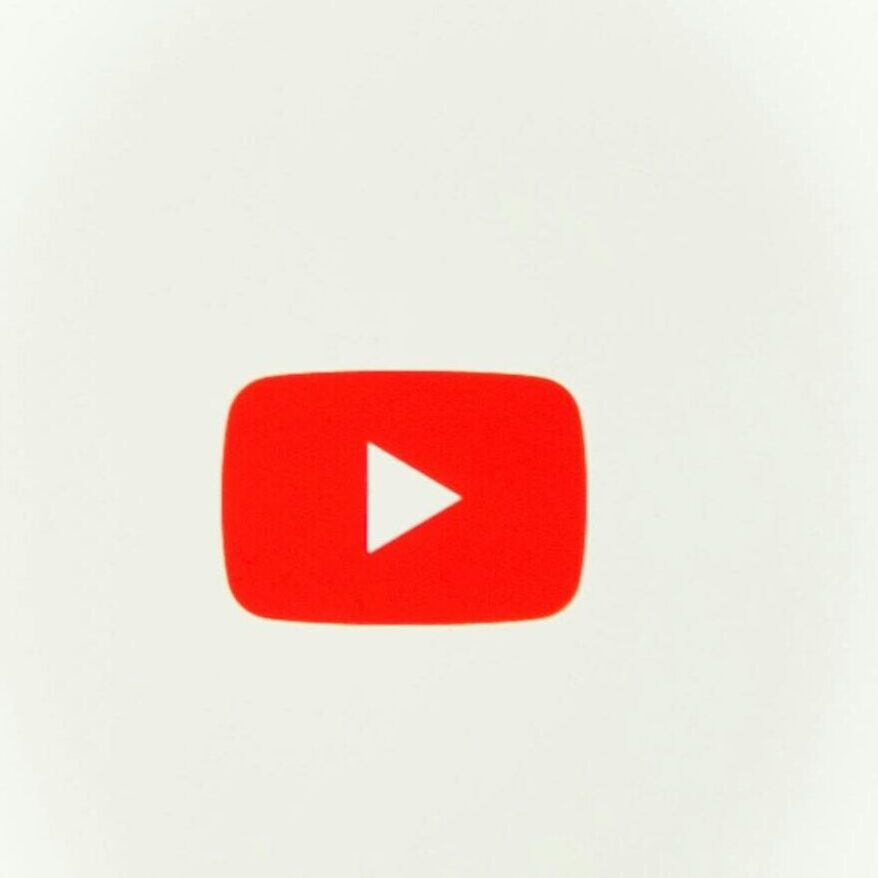 A hand holding a smartphone displaying the YouTube app against a red background.